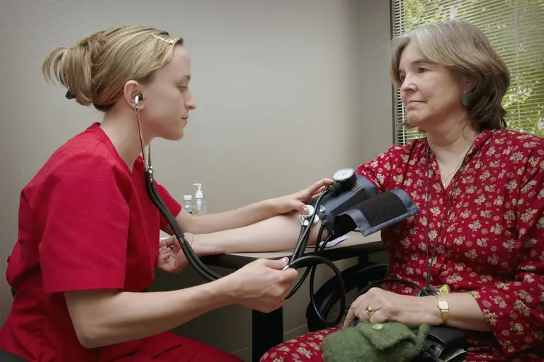 A nurse in red scrubs taking an older woman's blood pressure